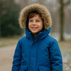 Parka enfant sur un enfant souriant avec capuche fourrée en extérieur.