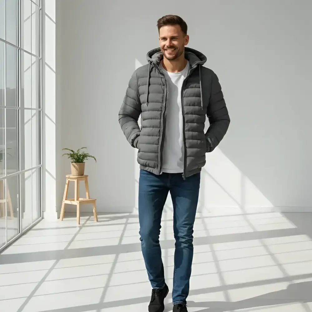 Homme portant une parka doudoune homme légère en gris, avec un sourire, dans un intérieur lumineux.