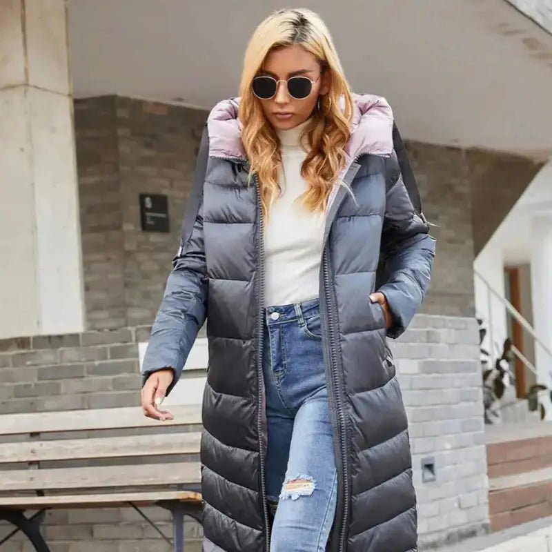 Parka femme à capuche longue modèle gris avec doublure rose, portée par une femme à lunettes de soleil.