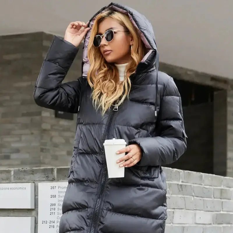 Femme portant une parka femme à capuche longue en gris, avec un gobelet à emporter.