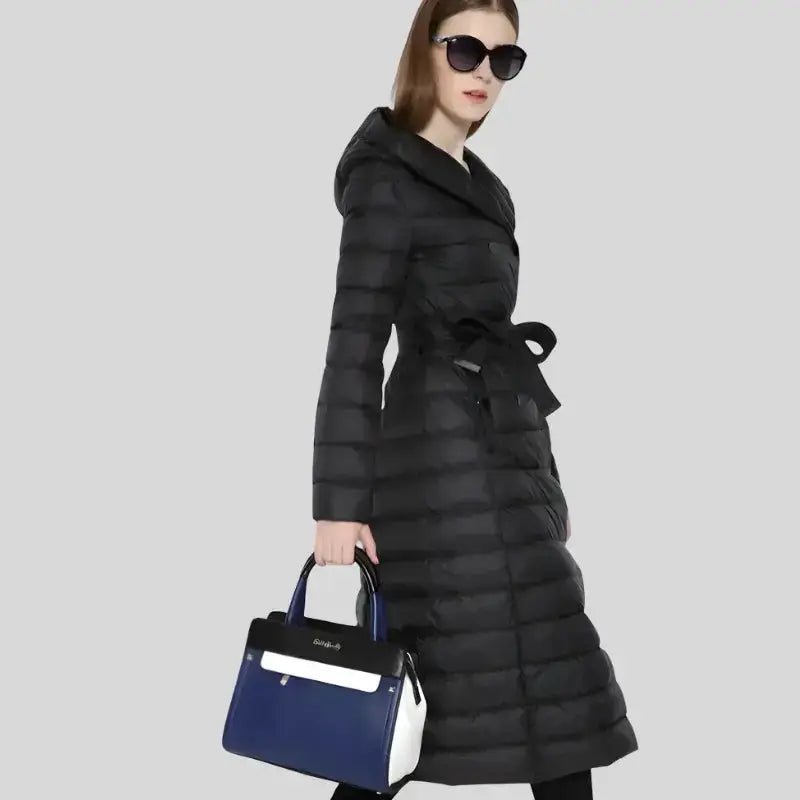 Parka femme longue à capuche noire, modèle avec ceinture, portée avec un sac à main élégant, look hivernal.