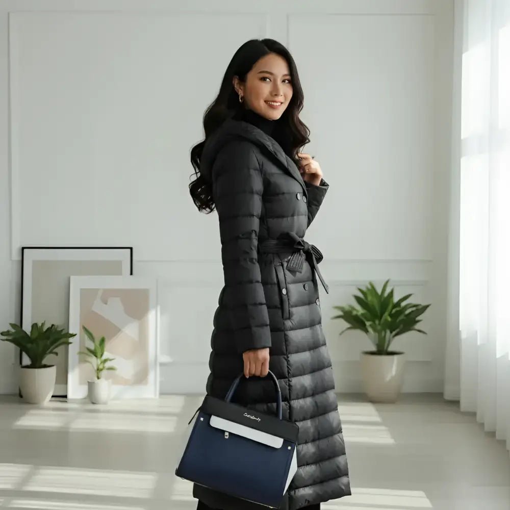 Parka femme longue à capuche noire avec ceinture portée par une femme dans un intérieur moderne.