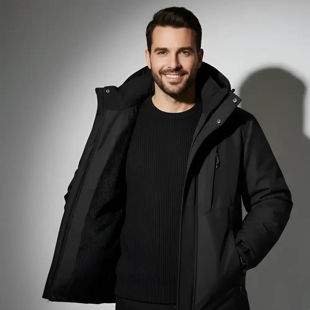 Homme souriant portant une parka homme bicolore à capuche ouverte sur un pull noir, avec un fond neutre.