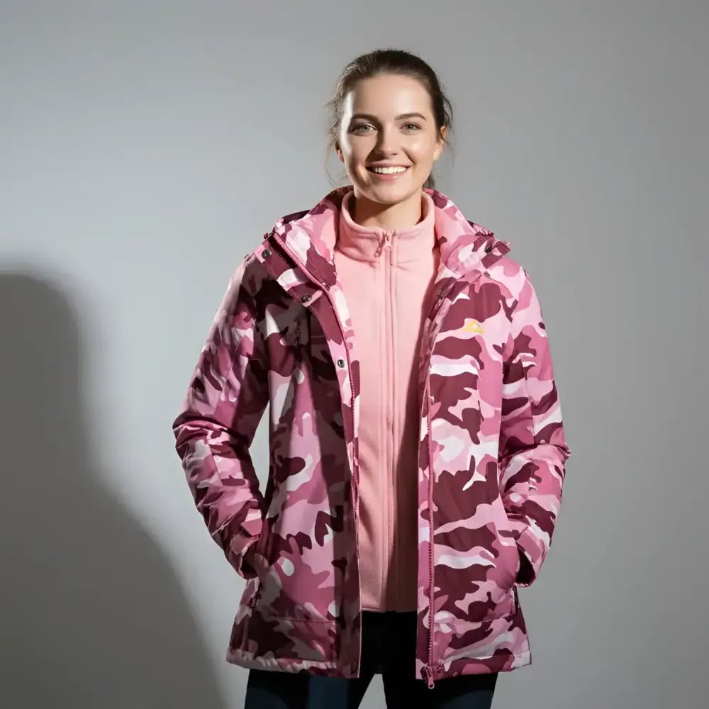 Femme en parka femme colorée rose camouflage avec capuche, souriante sur fond gris.